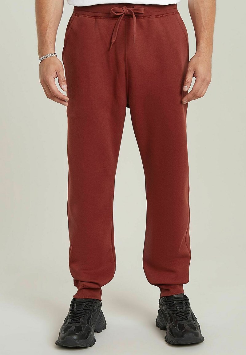 Bordeauxrode sweatpants van zacht materiaal, met een elastische taille met trekkoord, taps toelopende pijpen en zijzakken. G_dragen met zwarte sneakers.