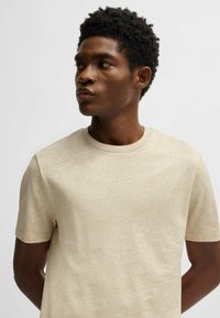 T-shirt beige a maniche corte realizzato in tessuto testurizzato, con scollatura a girocollo e vestibilità rilassata, indossato da un modello con capelli corti scuri.