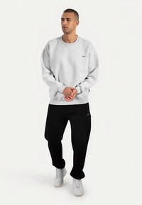 Grijze sweatshirt met een ronde hals en lange mouwen, gecombineerd met een zwarte broek. Draagt witte sneakers met een subtiele logodetail.