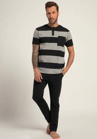 Gestreepte grijs en zwarte korte mouwen top met een kraag, knoopdetail en borstzak, gecombineerd met slanke zwarte broek. Glad stofgevoel.