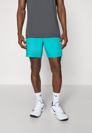 Shorts deportivos turquesa y camiseta sin mangas gris, llevados con zapatillas y calcetines blancos. Los shorts presentan un diseño de logo negro en el lateral.