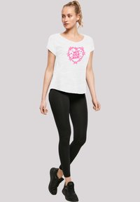 White short-sleeve t-shirt with pink "NOT YOUR BABE" graphic, paired with black leggings and black athletic shoes. Simple, relaxed fit.
