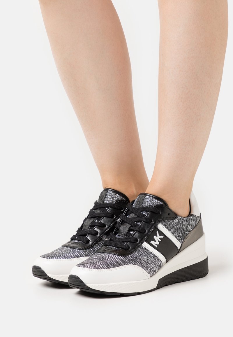 Sneaker con lacci che presentano una combinazione di materiale testurizzato nero e argento, una suola a zeppa e un accento logo audace sul lato.