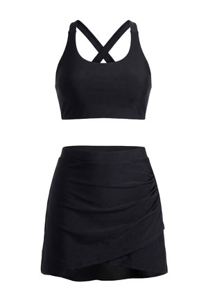 Costum sportiv negru din două piese, cu top scurt cu bretele încrucișate și fustă mini plisată cu talie înaltă și tiv asimetric.