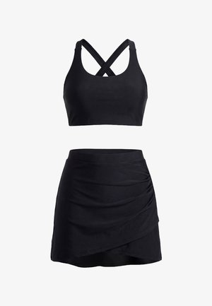 Schwarzes zweiteiliges Sportoutfit mit einem Crop-Top mit gekreuzten Trägern und einem hoch taillierten Minirock mit asymmetrischem Saum und Raffungen.