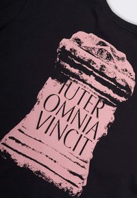 T-shirt nera con una grande grafica rosa di una colonna con il testo "IUTER OMNIA VINCIT", che mostra dettagli testurizzati e un design audace.