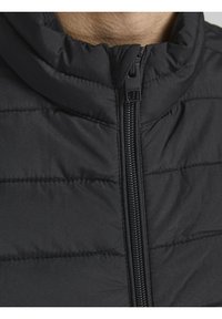 Czarna puchowa kurtka z wysokim kołnierzem, widocznym przeszyciem i zamkiem błyskawicznym z przodu. Tkanina wydaje się gładka z delikatnym połyskiem.