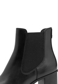 Černá kožená kotníková bota s elastickými bočními panely, zaoblenou špičkou a blokovým podpatkem. Hladký povrch s viditelným prošitím.