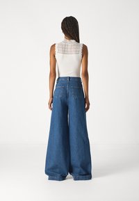 Bílý top bez rukávů s krajkovými detaily na zádech, spárovaný s oversized modrými džíny z denimu s zadními kapsami a vysokým pasem.