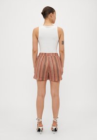 Pantaloni corti a righe in tessuto rosa, arancione e bianco con un elastico in vita. Abbinati a un top senza maniche bianco e tacchi con cinturini.