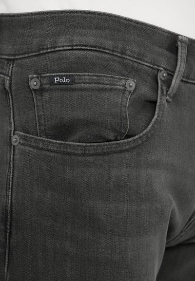 Tumed hall denim püksid, millel on silt "Polo", tagumine tasku, metallnupud ja sile tekstuur.
