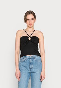 Top cropped preto com texturização em forma de canalé e detalhe em forma de olho de fechadura no centro, apresentando alças finas ajustáveis. Combinado com jeans de cintura alta em azul claro.