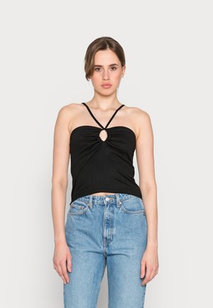 Top cropped preto com texturização em forma de canalé e detalhe em forma de olho de fechadura no centro, apresentando alças finas ajustáveis. Combinado com jeans de cintura alta em azul claro.