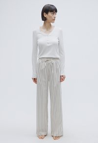 Haut henley à manches longues gris clair avec boutons, associé à un pantalon ample rayé blanc et noir avec une taille à cordon.