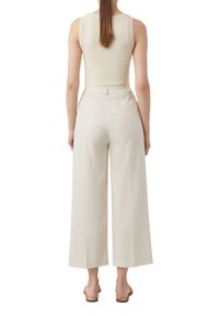 Beżowy top na ramiączkach z dzianinowym detalem na ramionach zestawiony z szerokimi beżowymi spodniami z bocznymi kieszeniami i dopasowanym krojem.