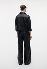 Zwarte leren cropped jack met brede mouwen, gecombineerd met hooggewaakte, wijde broek. Glad textuur, minimalistisch ontwerp, geen zichtbare hardware.