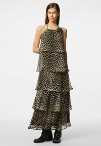 Robe maxi imprimée léopard avec volants superposés, décolleté halter et tissu léger. Présente une botte noire jusqu'à la cheville pour le contraste.
