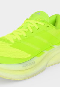 Chaussure de course jaune néon vif avec dessus en mesh, fermeture à lacets, trois bandes latérales et semelle blanche rembourrée portant la mention « Dreamstrike Glow ».