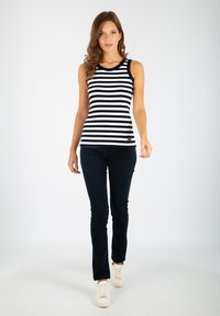 Czarny i biały, pasiasty top bez rękawów połączony z ciemnoniebieskimi spodniami i białymi trampkami. Top ma okrągły dekolt i dopasowany krój.