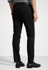 Svarta byxor med smal passform, med en jämn textur, diskret bakfickdetalj och skräddarsydd längd till ankeln. Bärs med svarta skor.