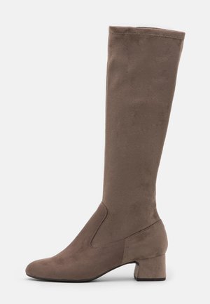 Botte marron en daim montant jusqu'au genou, avec un petit talon bloc, un bout rond, et des coutures minimales, présentée sur un fond blanc uni.