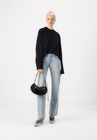 Crni oversized pulover, svijetle traperice ravnog kroja, cipele s srebrnim detaljima, crna lakirana torbica s patentnim zatvaračem, minimalistička pozadina.
