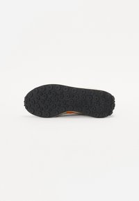 Black rubber shoe sole with circular traction patterns. Features a yellow accent and a smooth finish, designed for grip and durability.