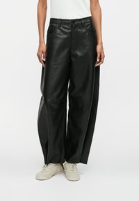 Zwarte leren wijde broek met voorzakken, een gladde textuur, zichtbare stikseldetails en gecombineerd met lichtgekleurde sneakers.