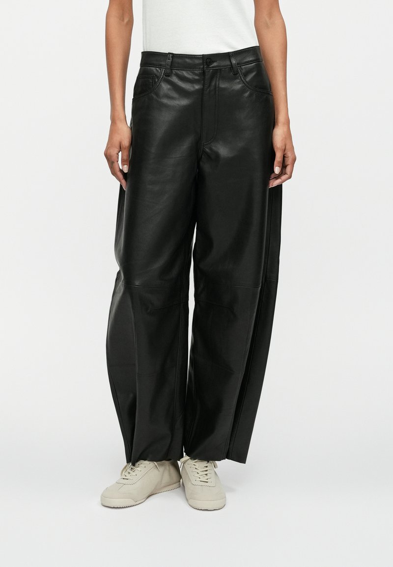 Zwarte leren wijde broek met voorzakken, een gladde textuur, zichtbare stikseldetails en gecombineerd met lichtgekleurde sneakers.