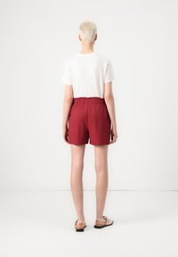 Shorts en coton rouges avec une taille haute et une bande élastique, associés à un t-shirt blanc. Des sandales complètent la tenue décontractée.