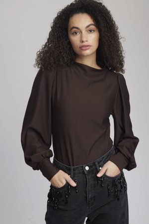 Brown long-sleeve top with puffed shoulders, paired with black jeans featuring beaded accents on the pockets. Smooth fabric texture.