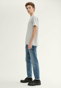 Camiseta de algodón gris de manga corta, combinada con jeans de mezclilla azul claro, arremangados en los puños, y zapatos negros con cordones.