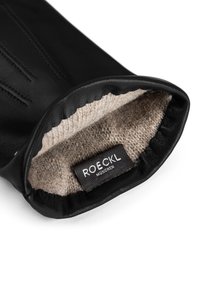 Black leather glove with beige wool lining visible, featuring a "ROECKL MUNICH" brand label inside the wrist opening.