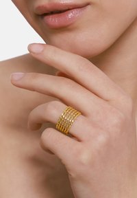 Anello multi-band in oro con texture intrecciata e bordi lisci, indossato su un dito, che mette in risalto la sua superficie riflettente e il design stratificato.