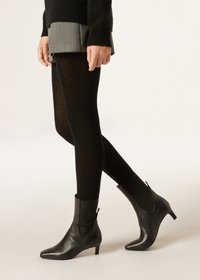 Czarne skórzane botki za kostkę z wysmukłą noskiem i obcasem 3 cm. Posiadają zamek błyskawiczny z boku oraz gładką fakturę, zestawione z czarnymi legginsami i szarym spódnicą.