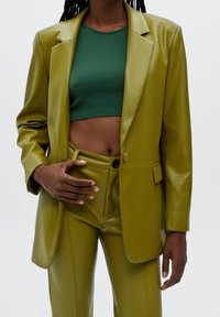 Grön konstläderblazer med en enda knäppning, kombinerad med matchande högmidjade byxor och en figurnära grön cropped top. Slät textur.
