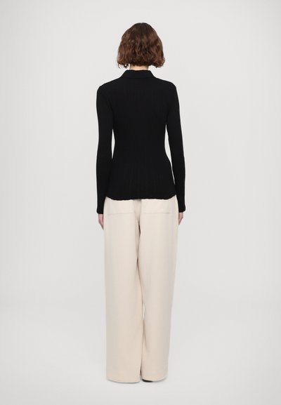 Schwarzes geripptes Strickoberteil mit langen Ärmeln, eng anliegender Silhouette und kragenlosem Ausschnitt, kombiniert mit weiten, cremefarbenen Hosen.