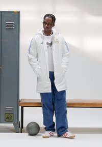White puffer coat with blue stripes, layered over a gray shirt, paired with baggy blue jeans and red-accented white sneakers. Black basketball nearby.