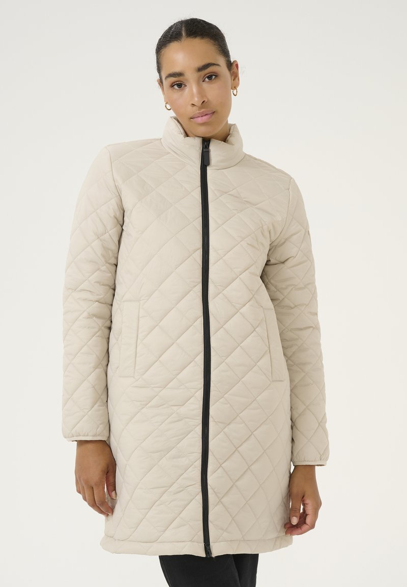 Beige kviltet jakke med høj krave, frontlynlås og sidelommer. Glat tekstur og diamantskærm i hele stoffet.
