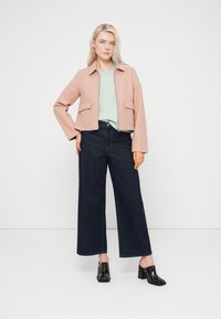 Ροζ ανοιχτό ροζ κοντό μπουφάν με γιακά και δύο μπροστινές τσέπες, συνδυασμένο με τοπ σε μέντα και σκούρο τζιν με φαρδιά μπατζάκια, ολοκληρωμένο με μαύρα mules με τακούνι.