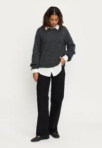 Grijze wollen trui over een witte blouse met kraag, gecombineerd met zwarte wijde broek en zwarte slippers. Casual, ontspannen pasvorm.