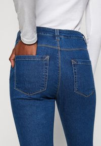 Vaqueros azules con un diseño de cintura media, dos bolsillos traseros con costuras en contraste y una textura de denim suave.