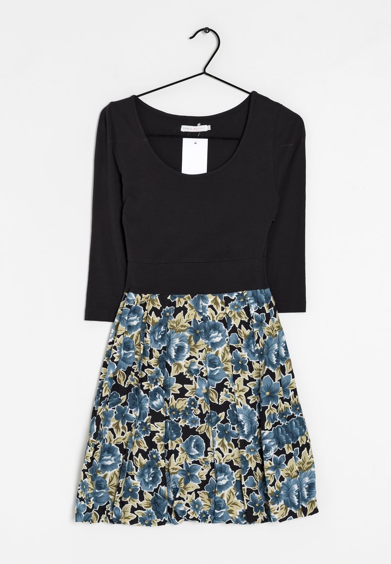 Svart långärmad topp med rund halsringning, kopplad till en blommig plisserad kjol med blå och gröna blommor på en svart bakgrund.