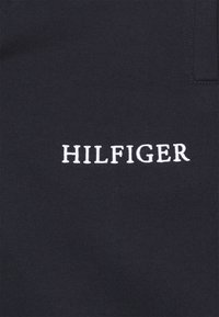 Granatowa bluza z białym, wyhaftowanym napisem "HILFIGER" na przodzie. Wykonana z miękkiego, teksturowanego materiału o klasycznym kroju.