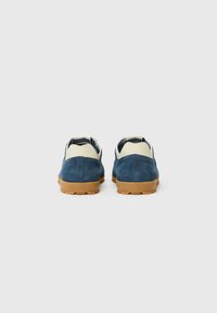 Blue suede shoes with a beige heel, featuring a gum rubber sole and a textured accent above the heel. Back view, no visible branding.