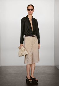 Schwarzes Hemd mit Knöpfen, beige Wildleder-Shorts, besetzter Gürtel, übergroße cremefarbene Clutch, schwarze Plateausandalen, glatte Texturen, neutrale Farbpalette.