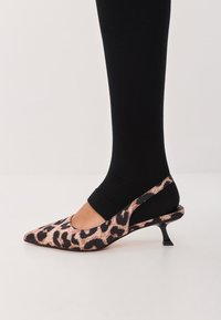 Leopard print slingback heel with a pointed toe, black fabric, and a slim black heel, worn with black leggings.
