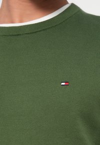 Πράσινο ριμπ πανωφόρι με λευκό γιακά. Διαθέτει ένα μικρό κεντημένο λογότυπο σε κόκκινο, λευκό και μπλε στο στήθος. Μαλακή υφή.