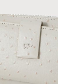 Light beige textured leather wallet featuring embossed dots, a flat strap closure, and logo detail on the front. Zippered top edge.