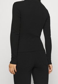 Black long-sleeve top crafted from a smooth, stretchy fabric, featuring a fitted design and subtle ribbed texture, shown from the back.
